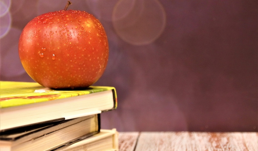 Мокрое яблоко на столе с книгами