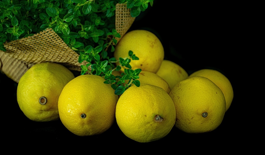 Желтые лимоны на черном столе с зеленью