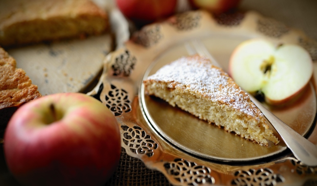 Кусок пирога с сахарной пудрой на столе с яблоками