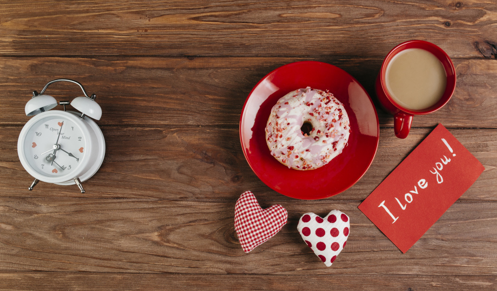 Пончик на столе с будильником, чашкой кофе и сердечками