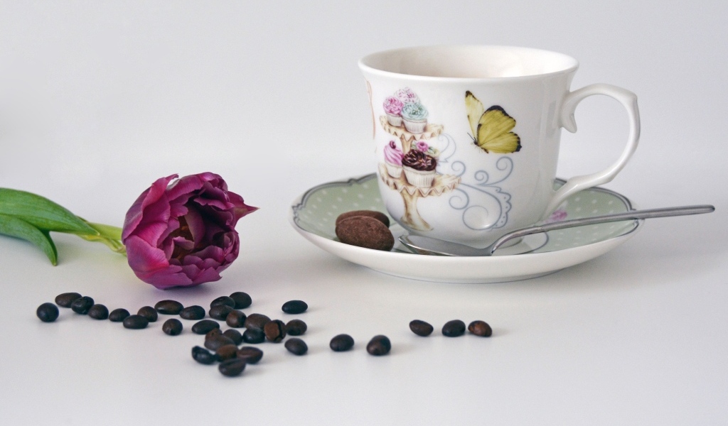 Чашка на столе с кофейными зернами и тюльпаном