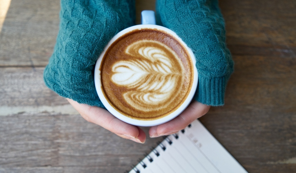 Горячая чашка кофе на столе в руках девушки