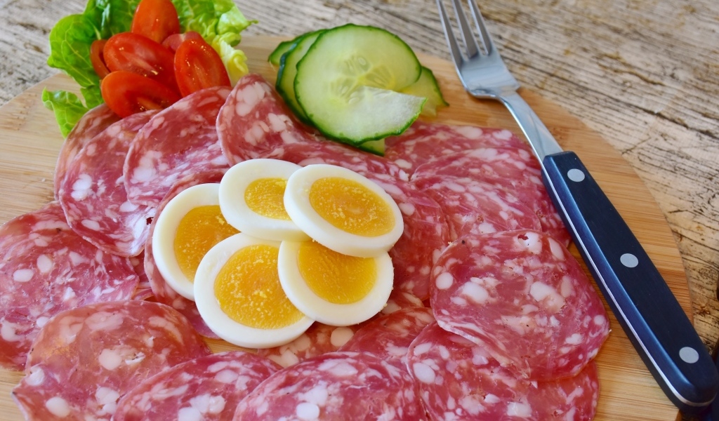 Колбаса салями на доске с вареными яйцами и овощами