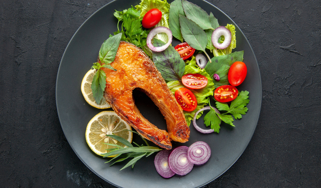 Жареная рыба на тарелке с зеленью,  лимоном и помидорами