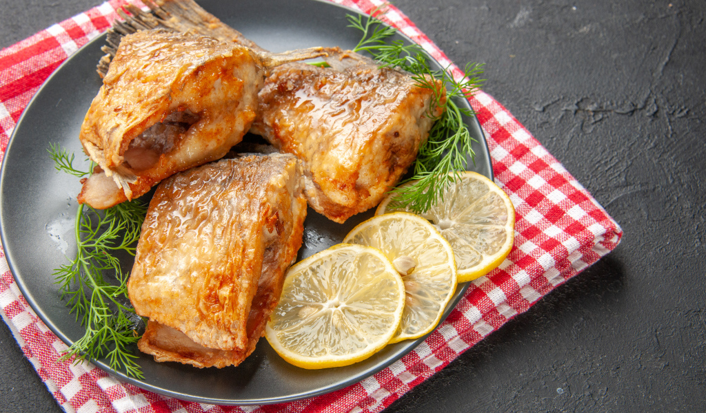 Куски жареной рыбы на тарелке с кусочками лимона и укропом