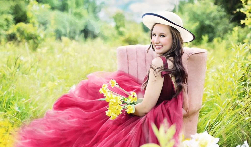 Красивая девушка в розовом платье сидит на кресле в траве