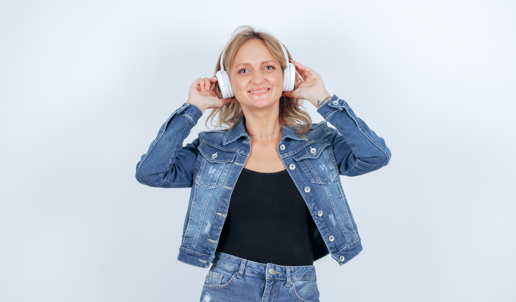 Девушка в джинсовом костюме с наушниками на голове на фоне стены