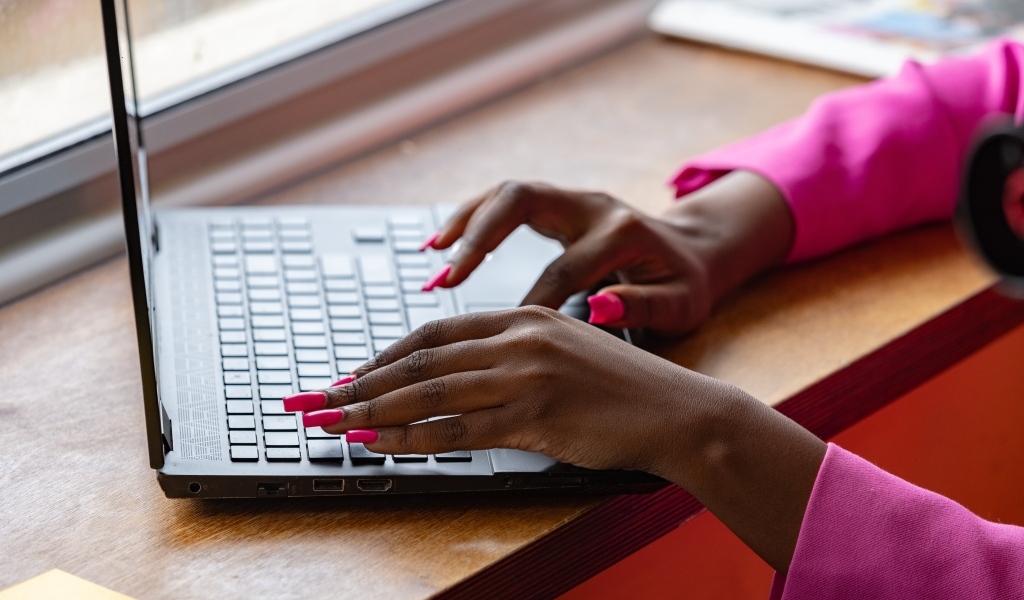 Девушка с розовым маникюром сидит за ноутбуком