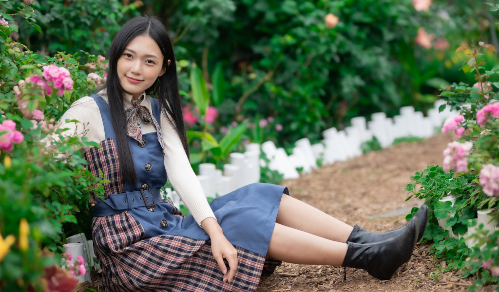 Молодая девушка сидит на тропинке у клумбы