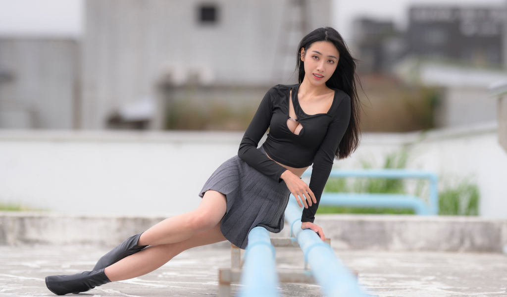 Девушка азиатка в черном наряде сидит на трубе