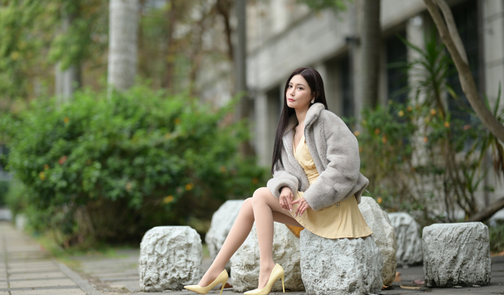 Азиатка в шубе сидит на квадратном камне