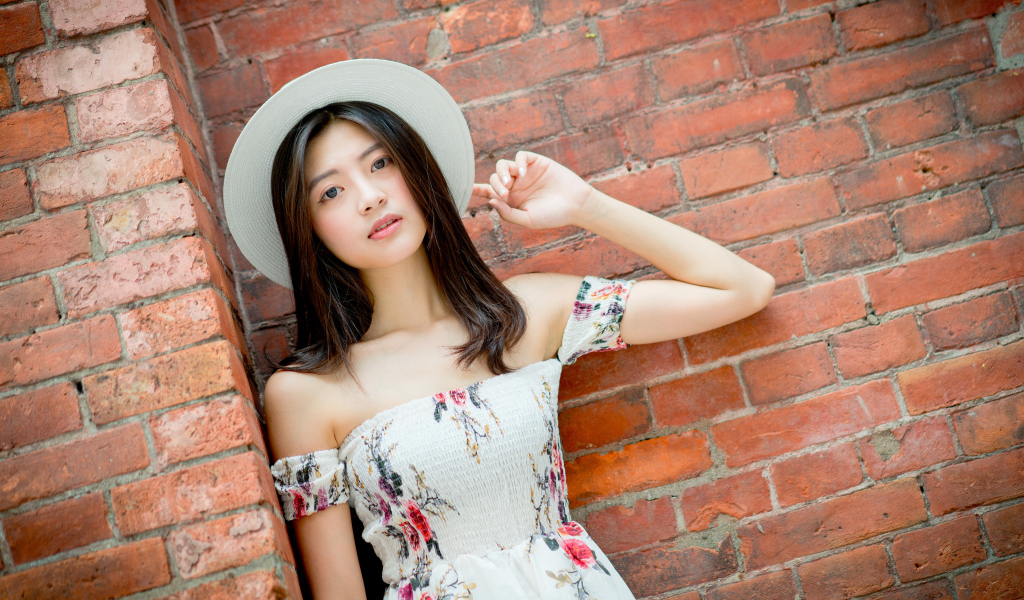 Азиатка в белой шляпе стоит у кирпичной стены