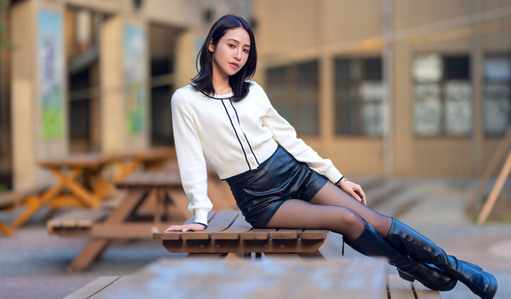 Азиатка в черных кожаных сапогах лежит на деревянном столе