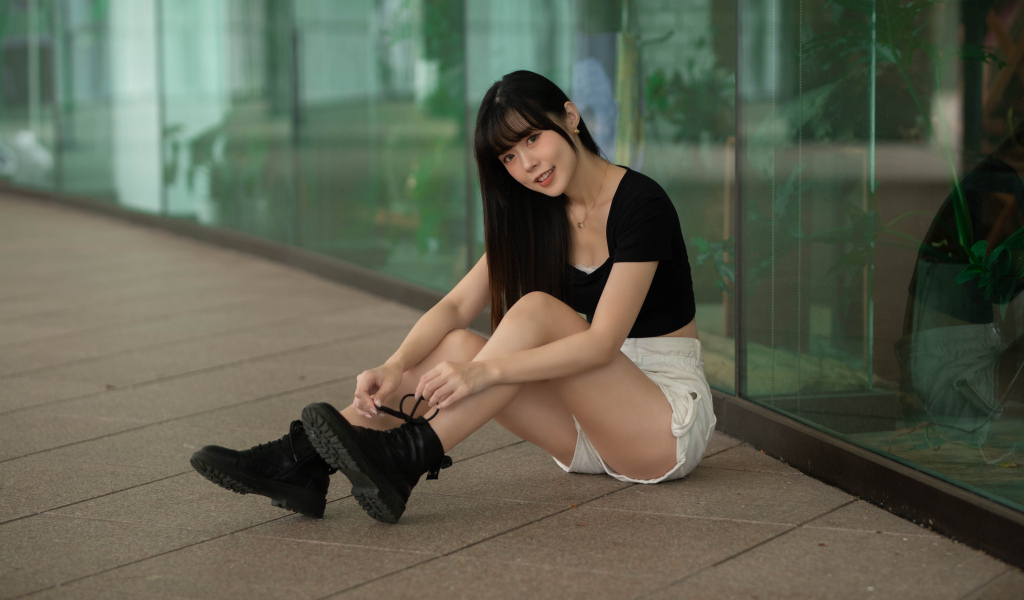 Азиатка в шортах сидит у стеклянной стены