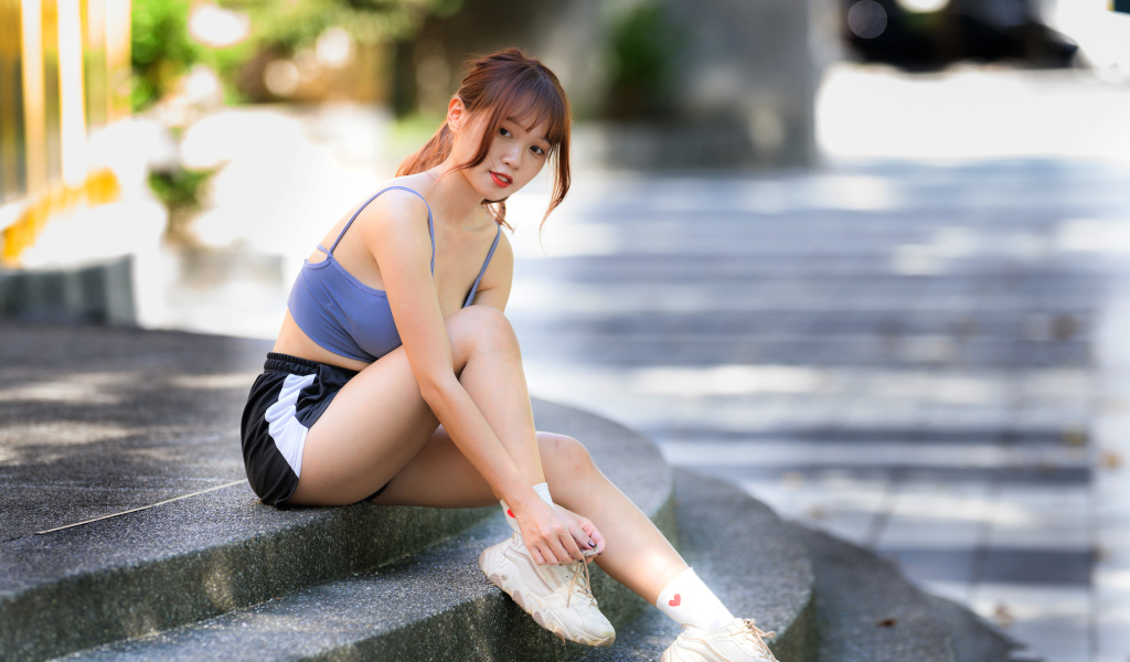 Азиатка в шортах сидит на ступеньках