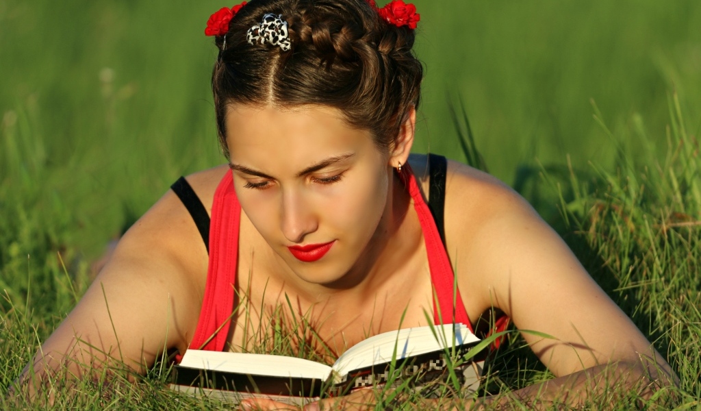 Красивая девушка читает книгу лежа на траве