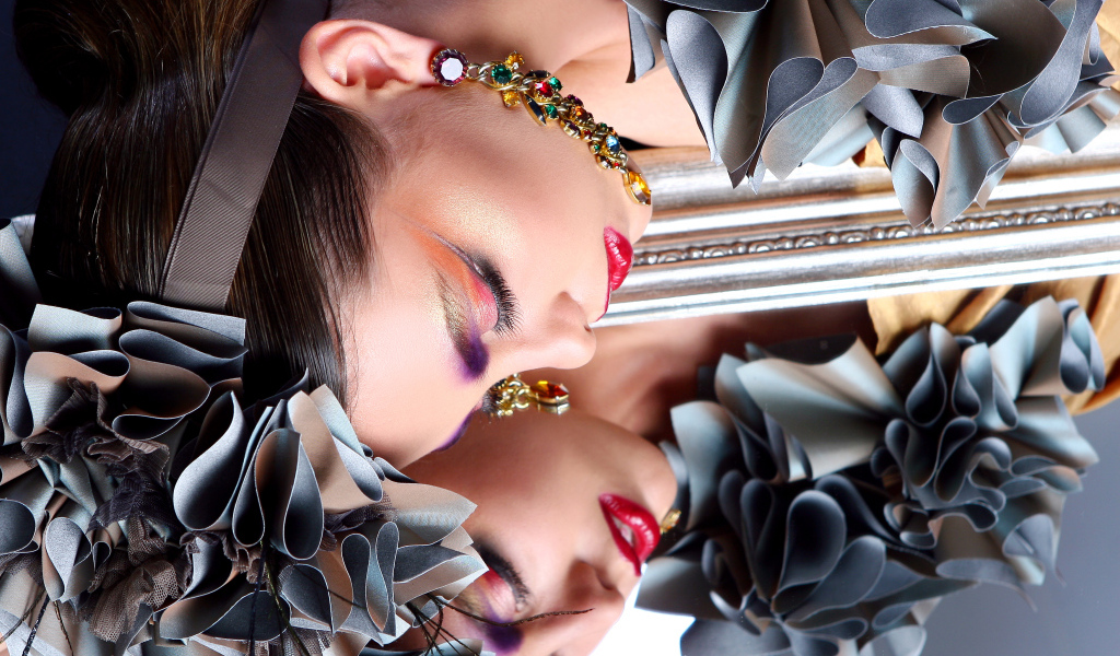 Красивая девушка с ярким макияжем отражается в зеркале