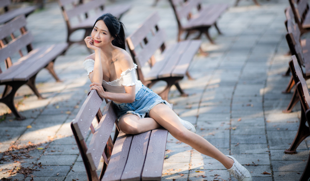 Милая девушка азиатка сидит на лавке в парке