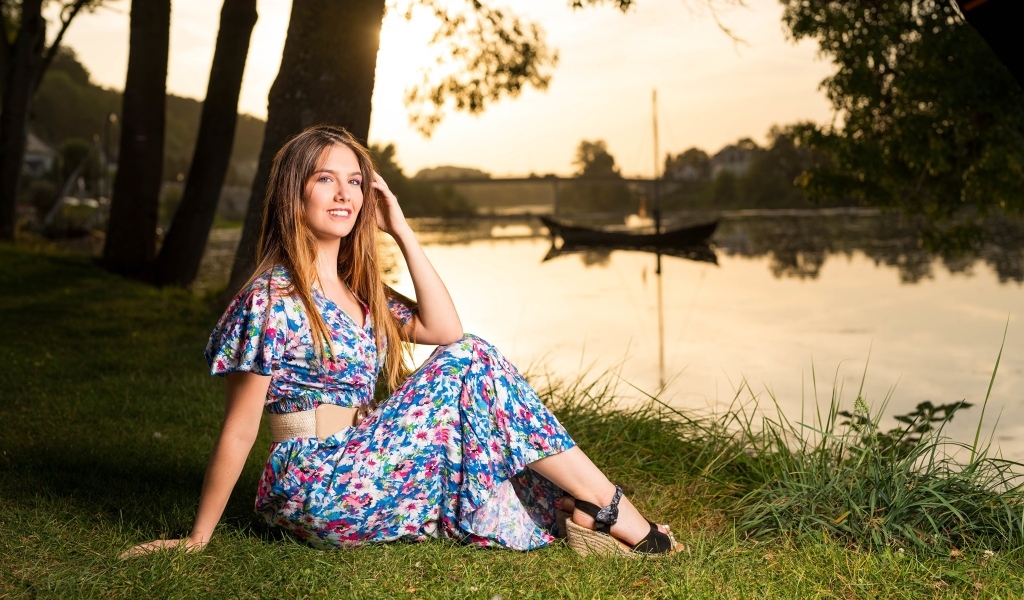 Милая девушка в платье сидит на берегу реки в парке