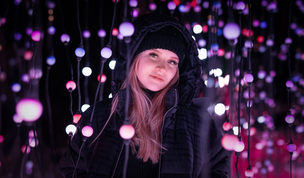 Девушка в черной куртке у светящейся гирлянды