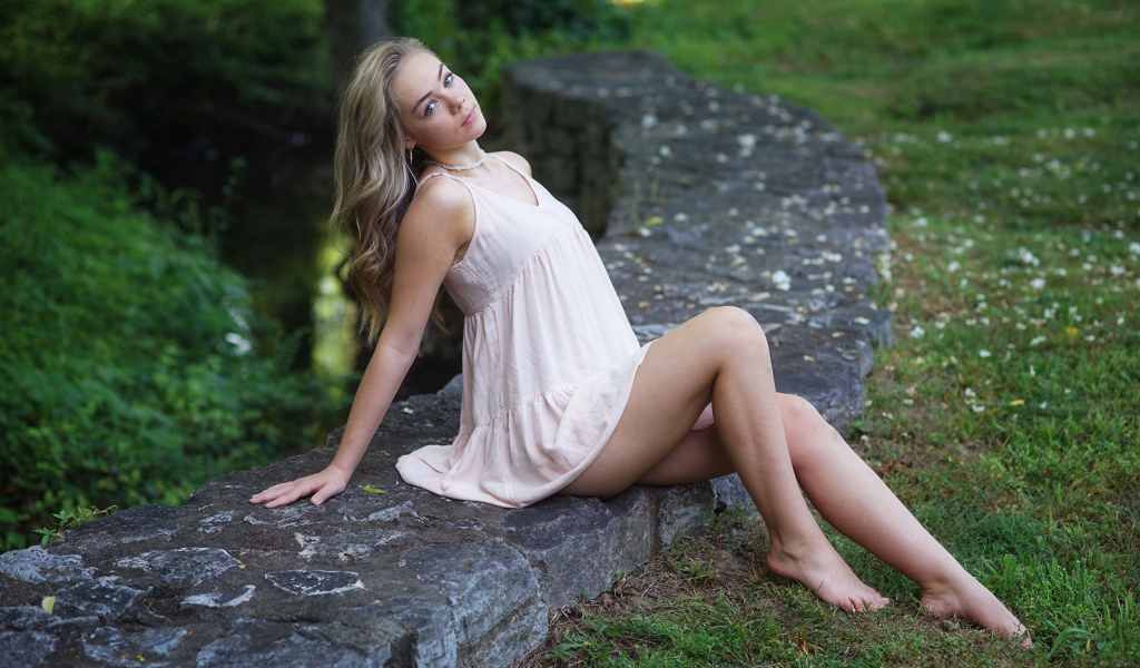 Длинноногая девушка сидит на камне в парке