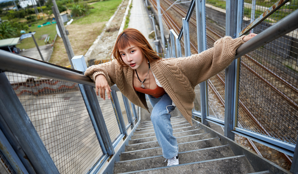 Рыжеволосая азиатка в кофте стоит на ступеньках