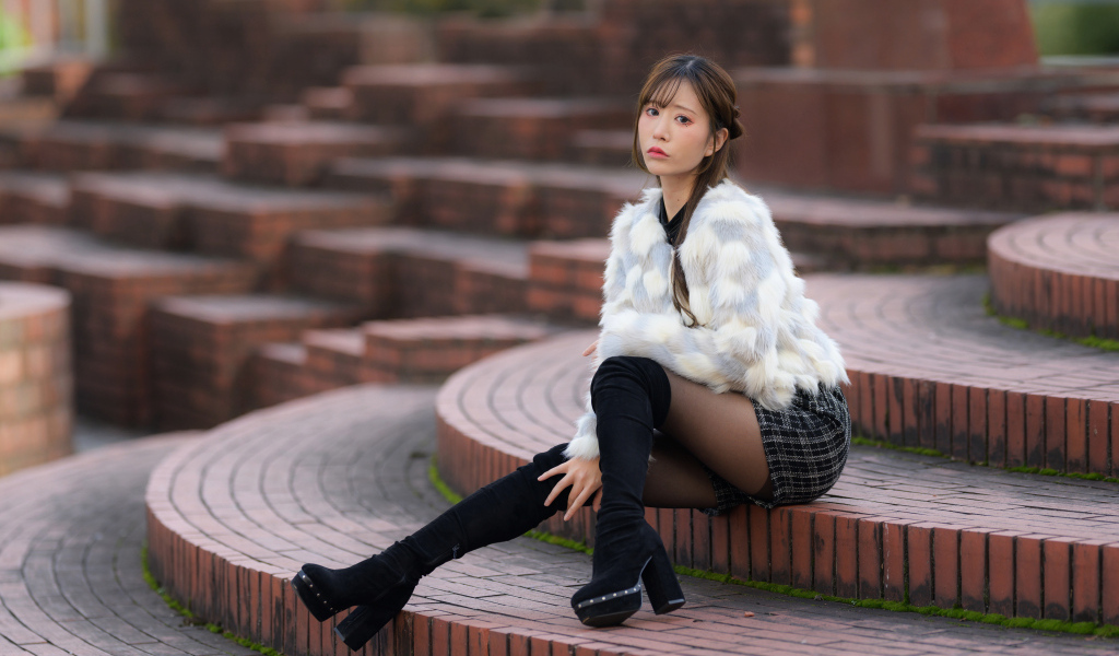 Грустная азиатка в шубе сидит на ступеньках
