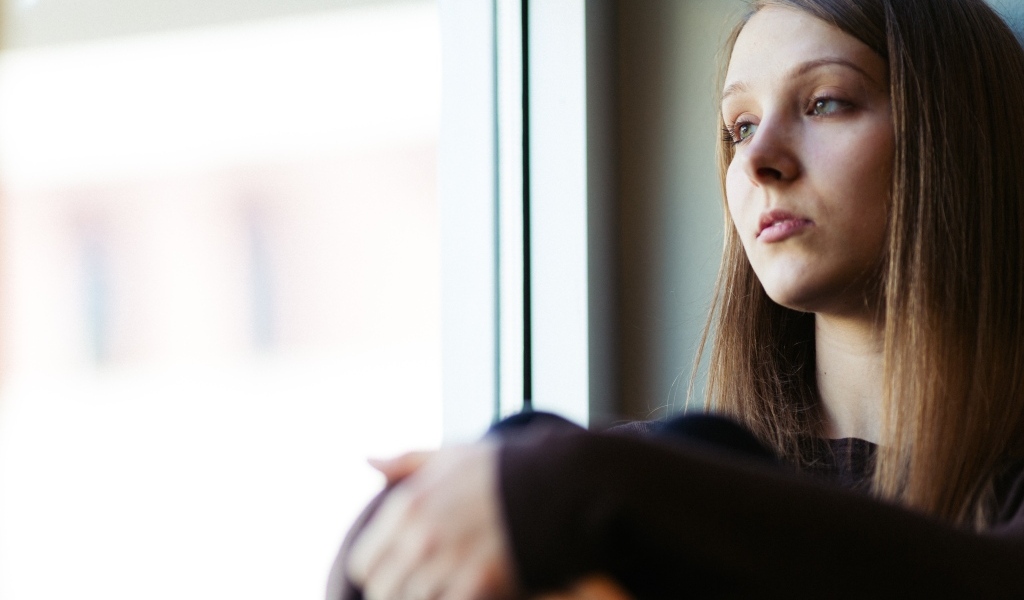 Грустная девушка сидит у окна