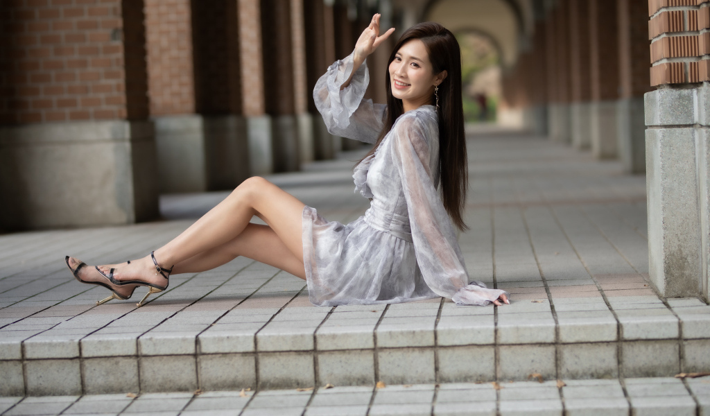 Улыбающаяся девушка азиатка сидит у ступеней