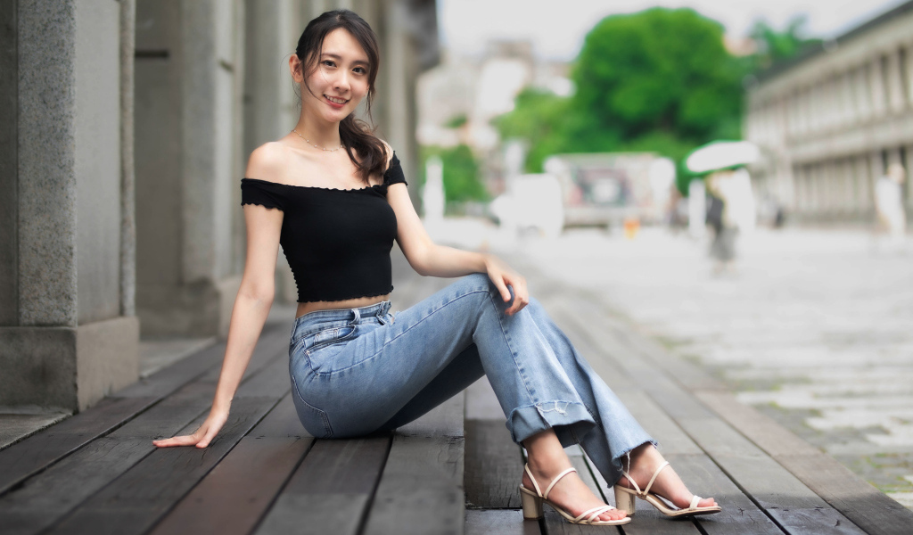 Улыбающаяся азиатка в джинсах сидит на пороге