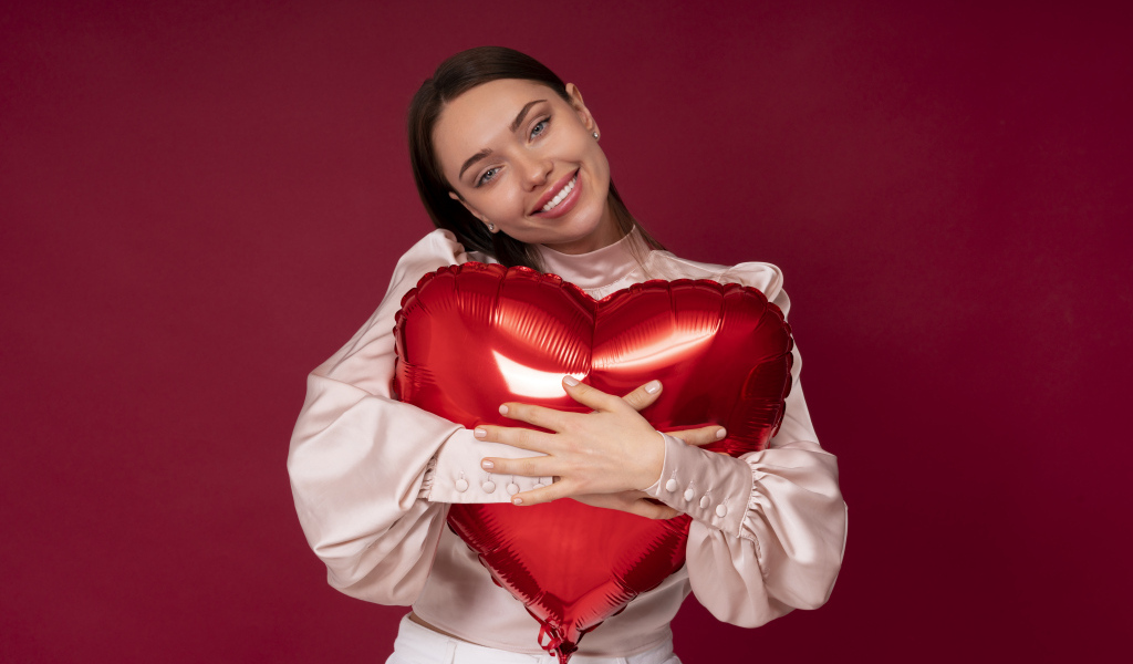 Улыбающаяся девушка обнимает шар в форме сердца