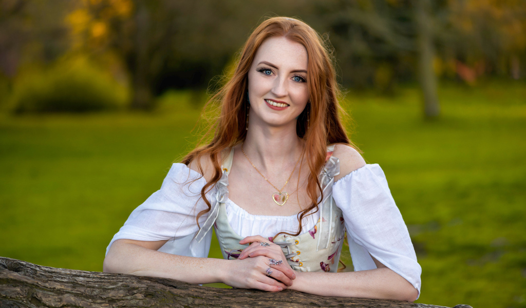 Улыбающаяся рыжеволосая девушка стоит у дерева
