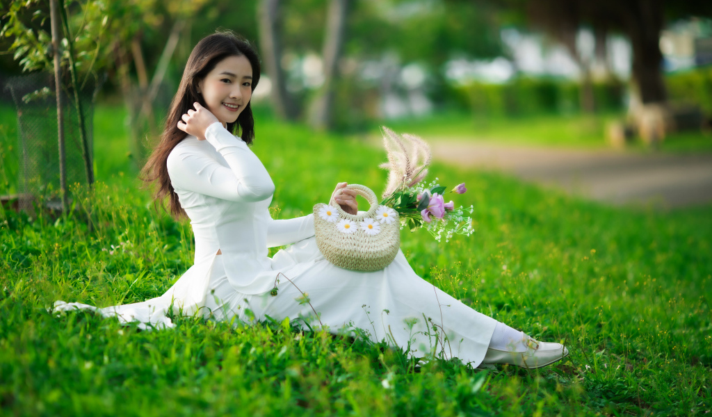 Нежная азиатка в белом наряде сидит на траве