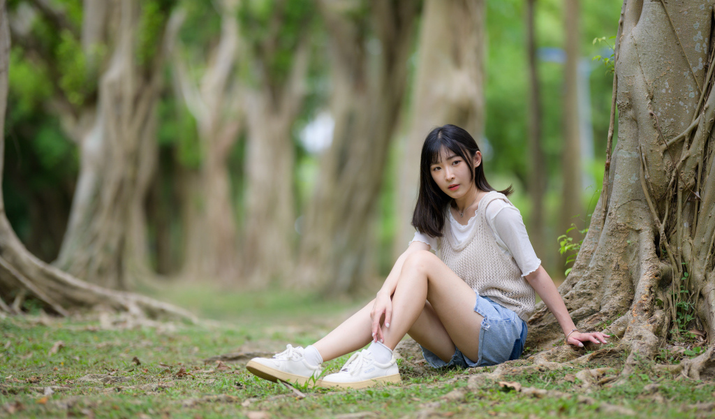 Молодая девушка азиатка сидит у дерева в парке