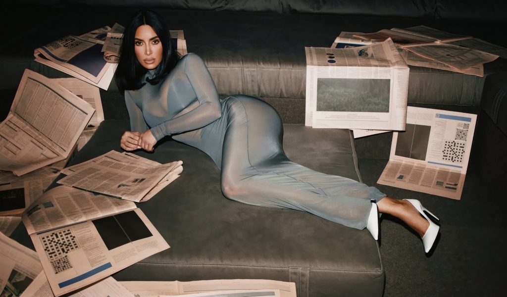 Модель Ким Кардашьян лежит на диване с газетами