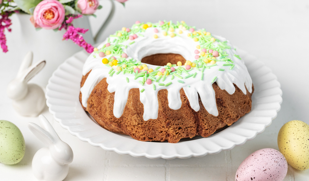 Сладкий пасхальный кулич с яйцами и цветами на столе