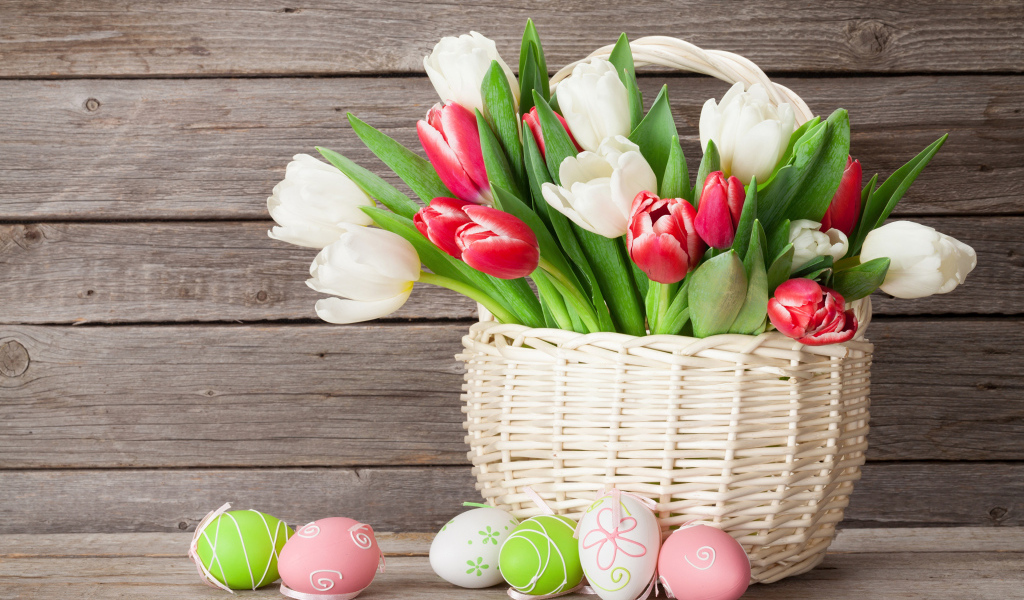 Белые и красные тюльпаны в корзине на столе с разноцветными яйцами на Пасху