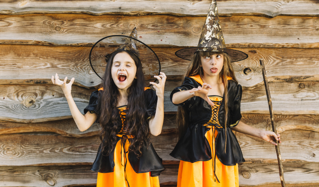 Две девочки в костюме ведьмы у стены на Хэллоуин
