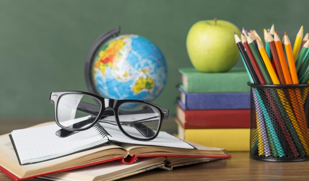 Книги, очки и карандаши с глобусом на столе у доски