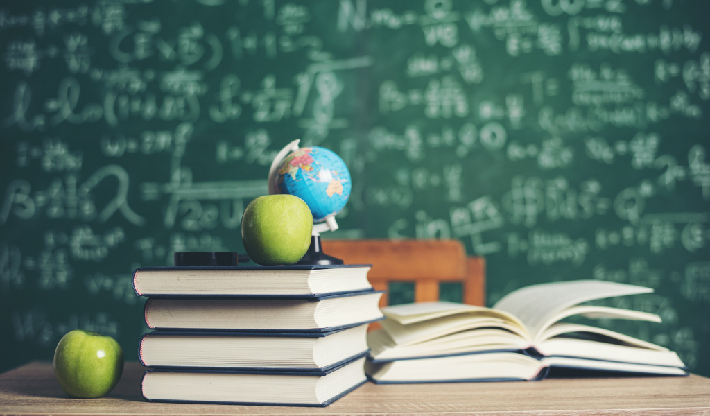 Книги на столе с зелеными яблоками и глобусом на фоне доски
