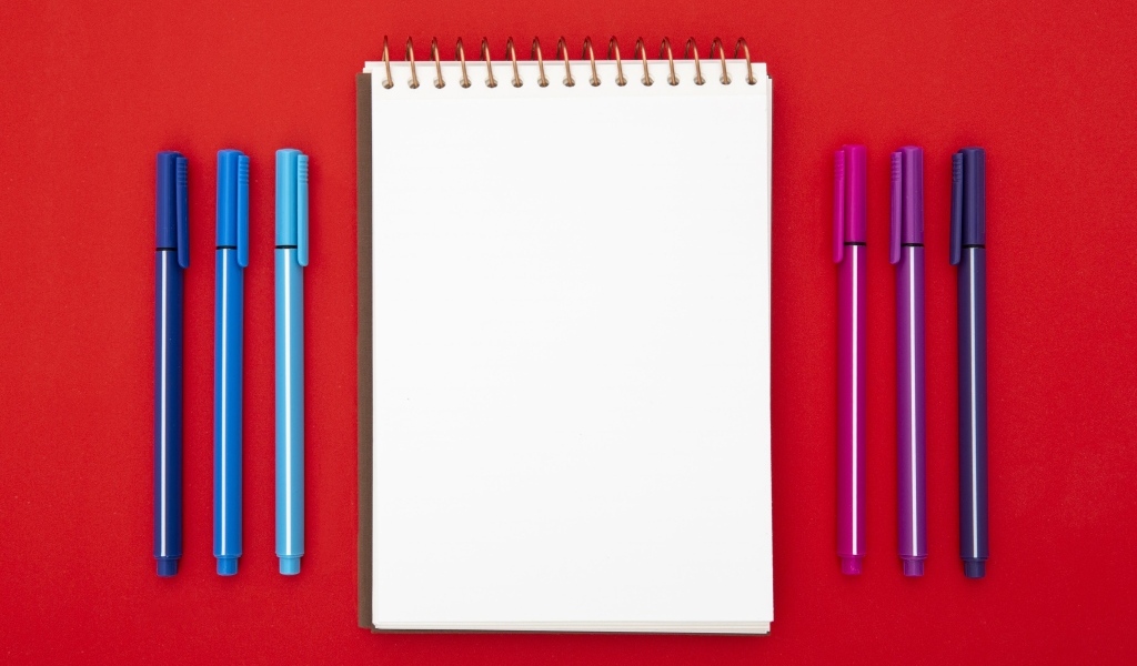 Блокнот и фломастеры на красном фоне