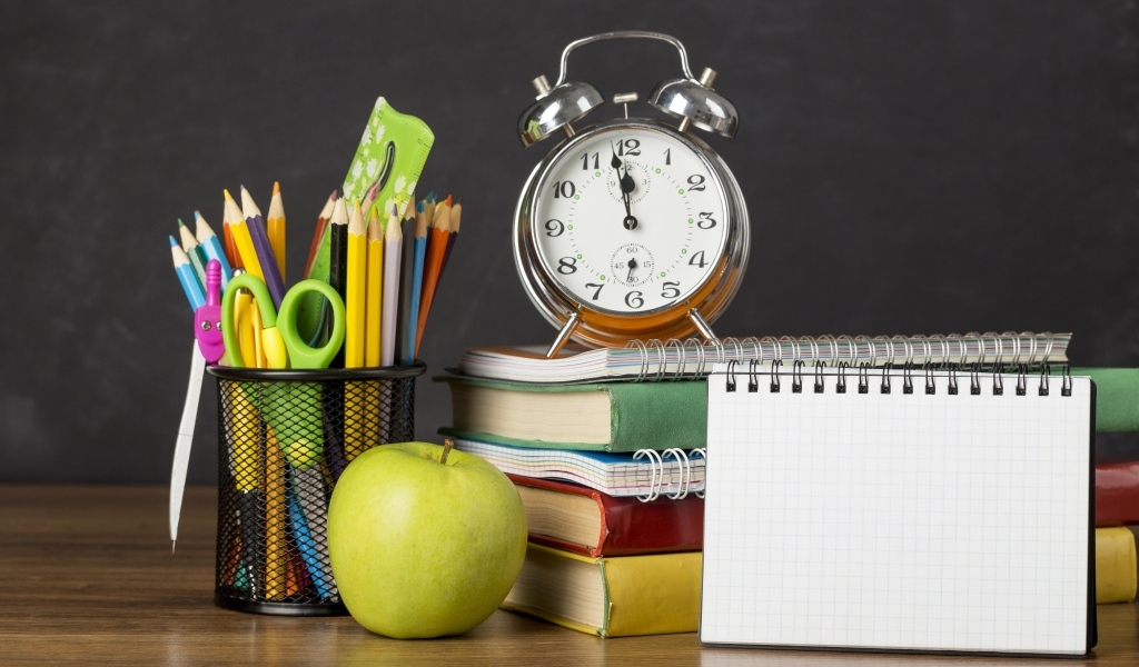 Канцелярские предметы на столе с будильником и книгами 