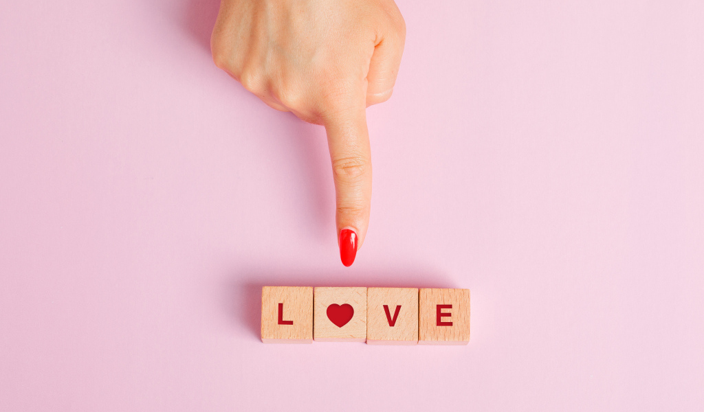 Рука указывает на кубики с надписью любовь на розовом фоне