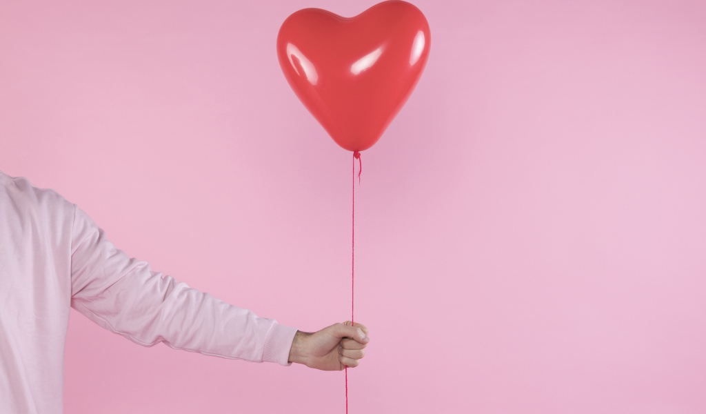 Шарик в форме сердца в руке на розовом фоне