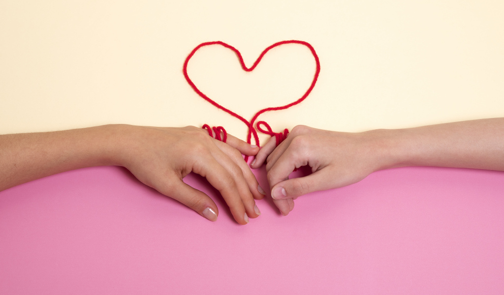 Человеческие руки связаны красной нитью в форме сердца