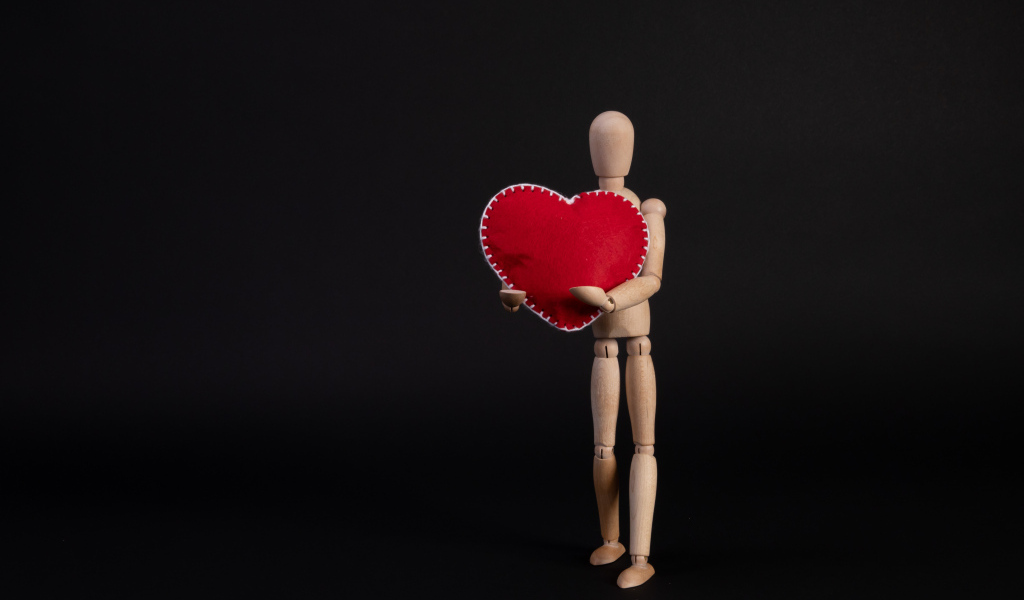 Марионетка держит красное сердце на черном фоне