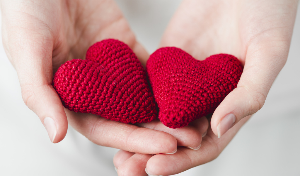 Два красных вязаных сердечка в руках девушки