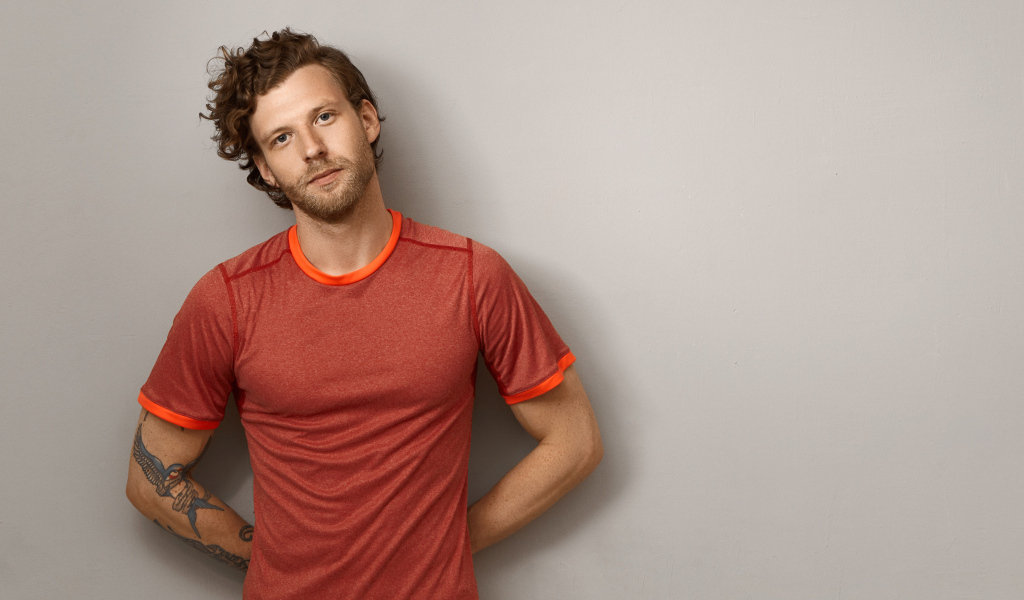 Мужчина в футболке стоит у серой стены