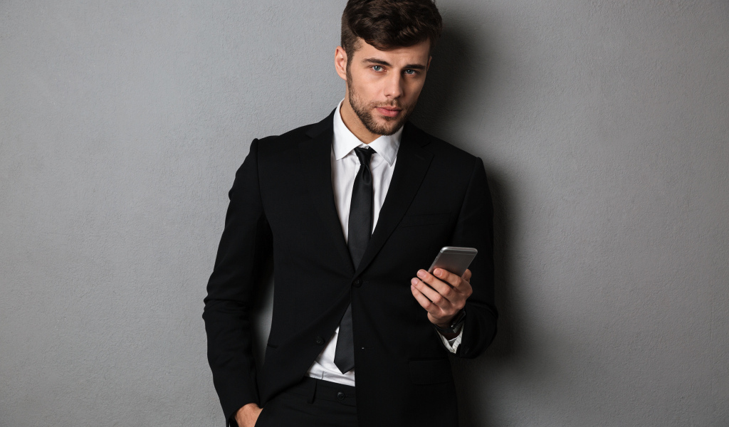 Деловой мужчина в костюме стоит у стены с телефоном