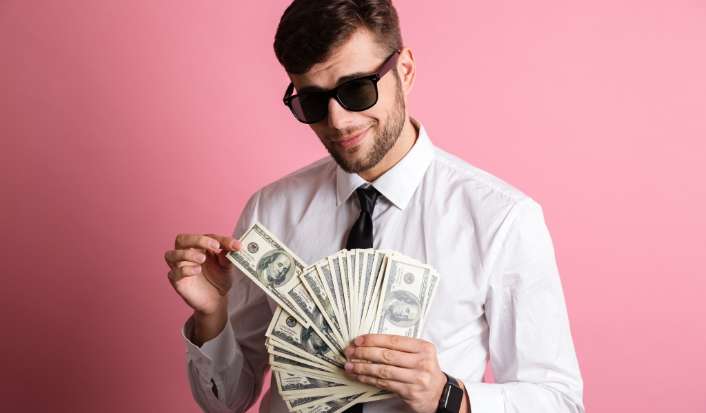 Деловой мужчина в черных очках с пачкой денег на розовом фоне